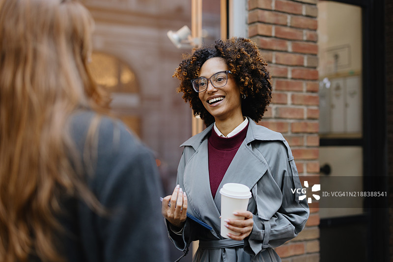 微笑的女商人与咖啡在城市环境中交谈图片素材