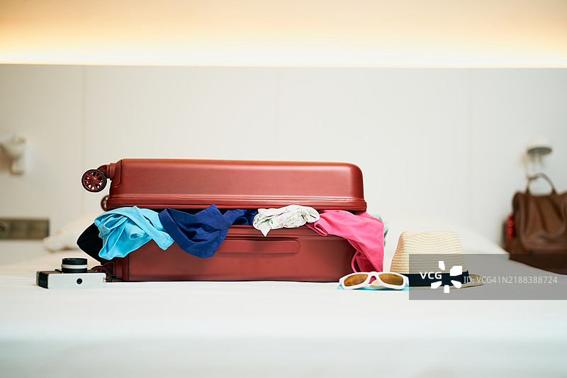 红色行李箱里满是衣物，放在酒店床上图片素材