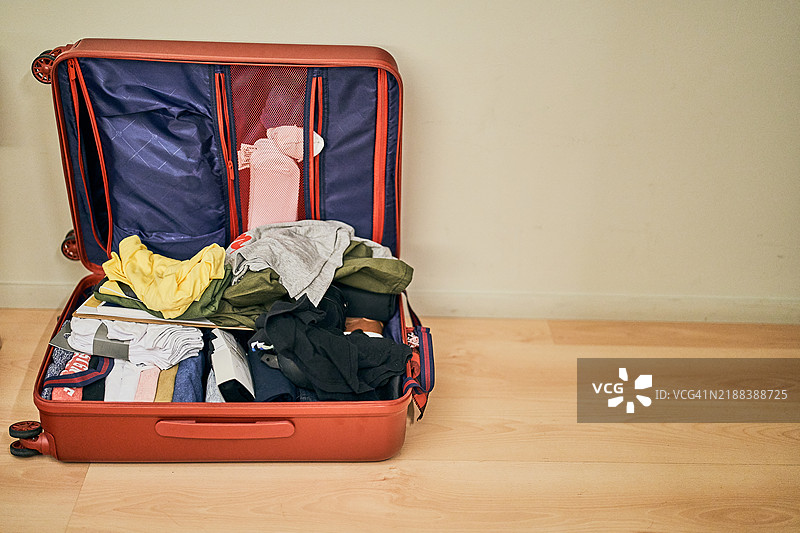 红色行李箱打开在地板上，里面衣物杂乱无章，准备出发旅行图片素材