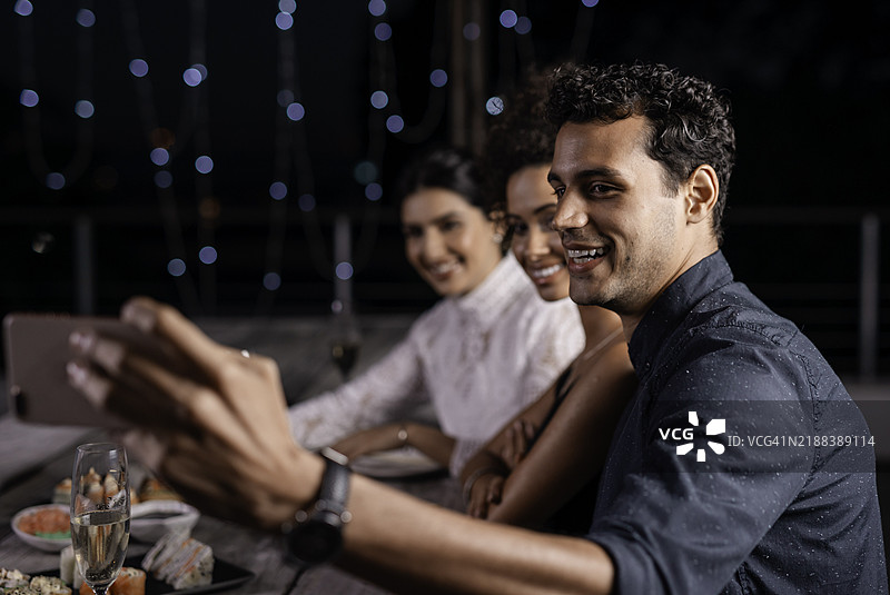朋友们在夜晚庆祝活动中享受精致的寿司晚餐，并用自拍记录下这一时刻图片素材