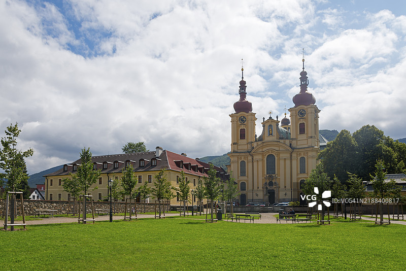 巴洛克风格的教堂，红色屋顶，周围环绕着树木和绿色草地，天空多云，位于捷克共和国利贝雷茨的海尼采，玛利亚探访修道院和朝圣教堂。图片素材