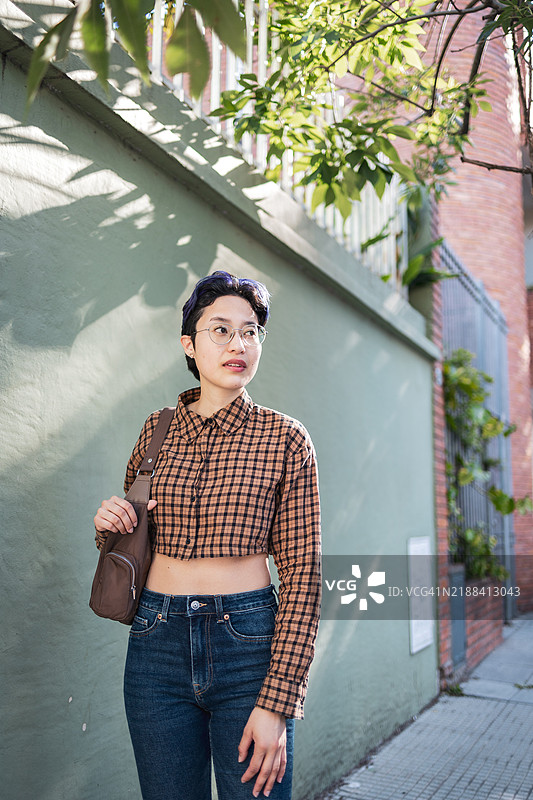 年轻人在阳光明媚的日子里站在人行道上，树荫下。图片素材