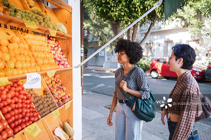 两个朋友在城市街道上的一个色彩斑斓的水果摊前探险图片素材