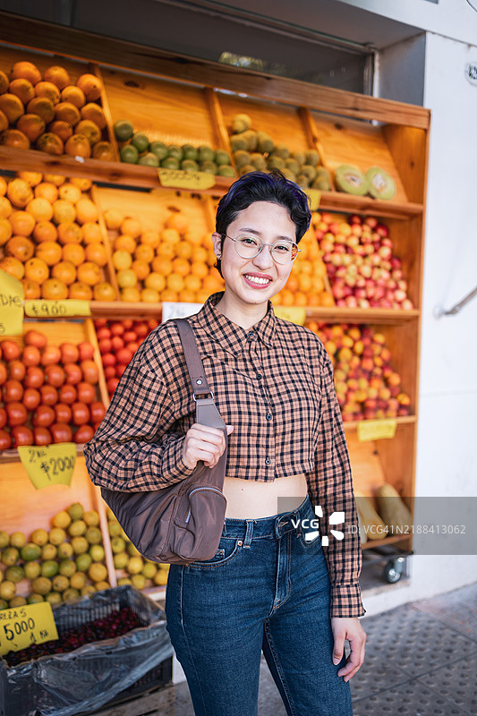 微笑的女性在当地市场摊位上购买新鲜水果图片素材