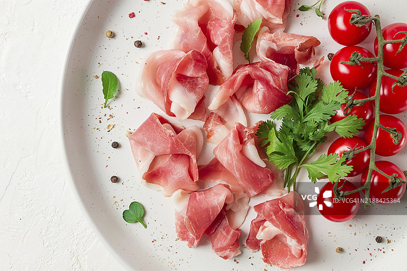 切片的意大利火腿，开胃菜，配樱桃番茄，放在白色盘子上，俯视图图片素材
