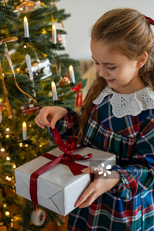 可爱快乐的小女孩在圣诞树旁拆礼物。冬季假期。图片素材