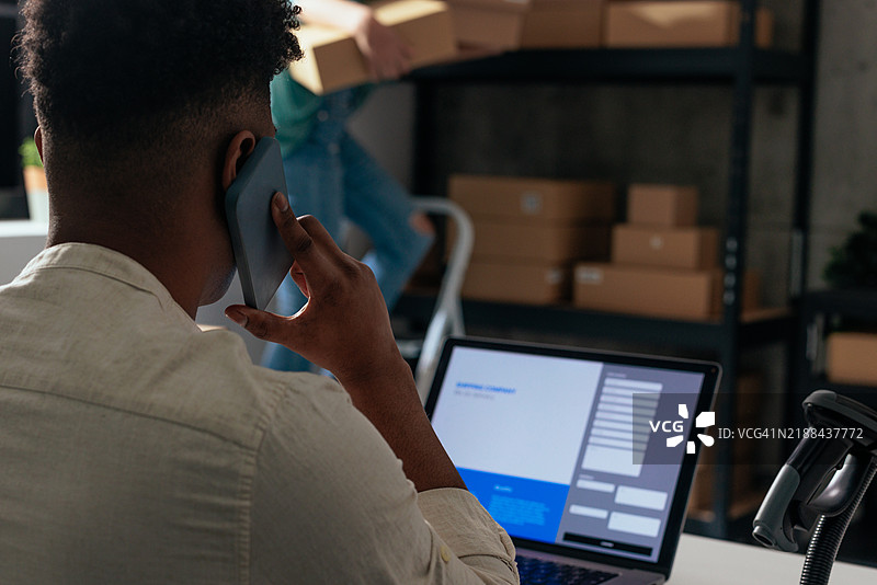 在办公室里，一名男子一边打电话一边使用笔记本电脑工作图片素材