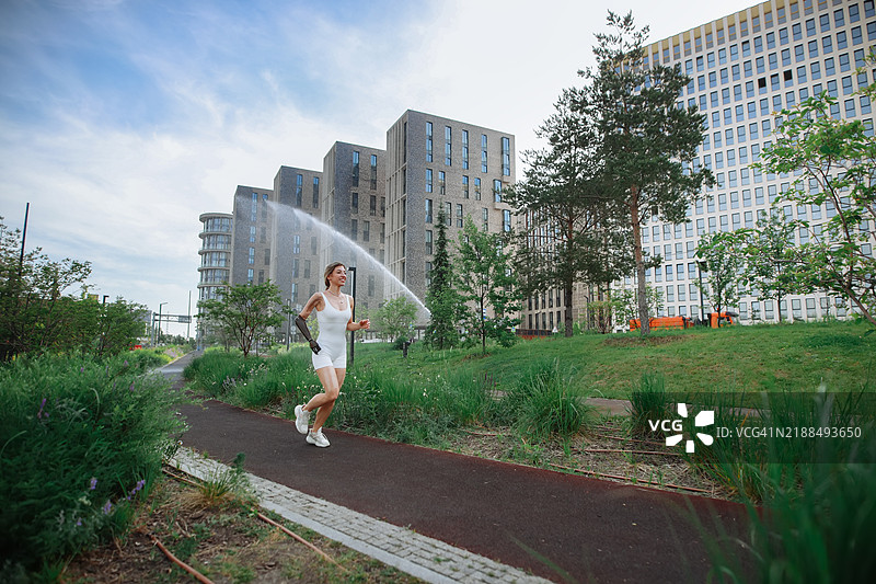 城市健康生活：美丽的女性在现代住宅区附近的公园里慢跑。图片素材