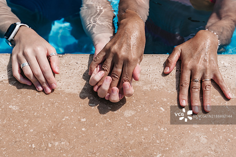 无法辨认的年轻女性和老年女性在游泳池中。双手放在池边，俯视图。图片素材