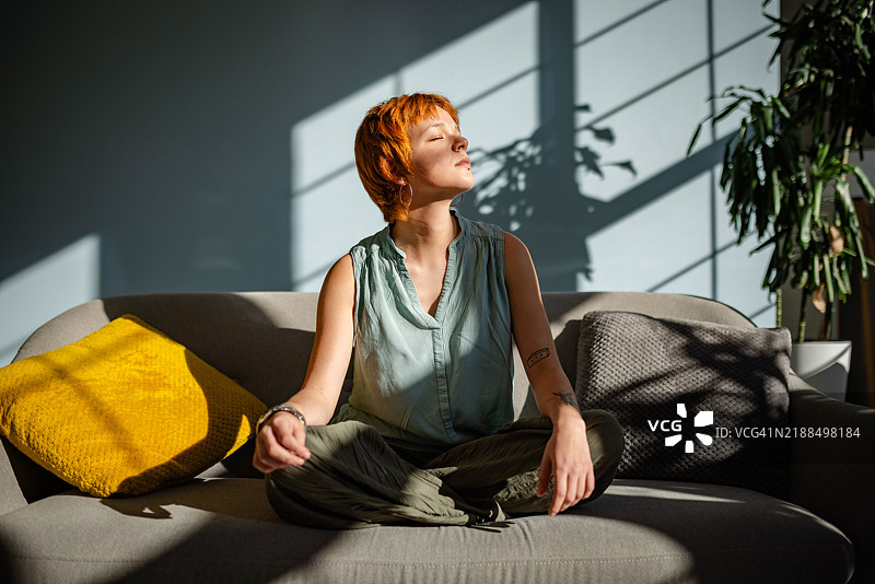 放松的女性在舒适的房间里沐浴在阳光下冥想。图片素材