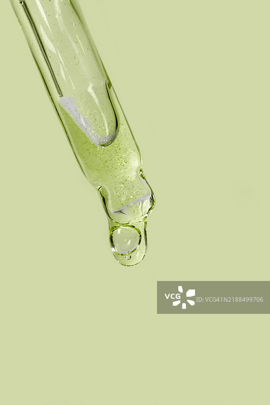 微距摄影。绿色实心背景上的玻璃移液管与面部精华。图片素材