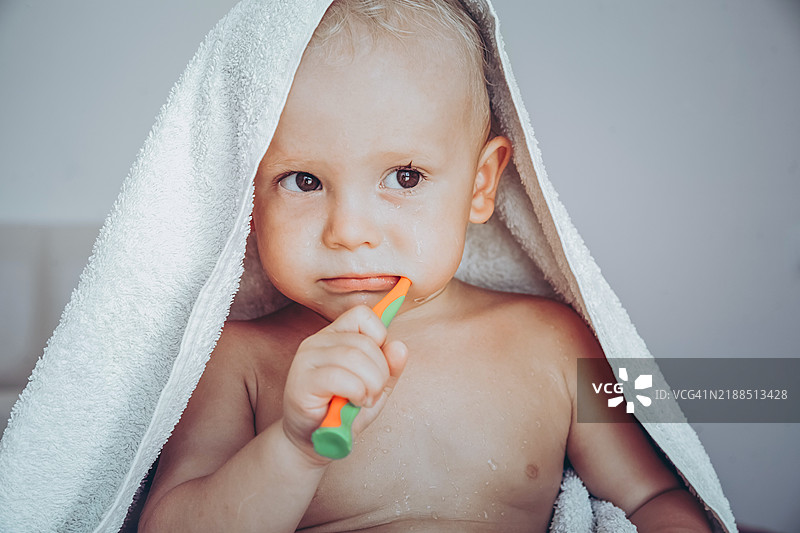 可爱的宝宝在温暖的毛巾下练习用牙刷刷牙。图片素材