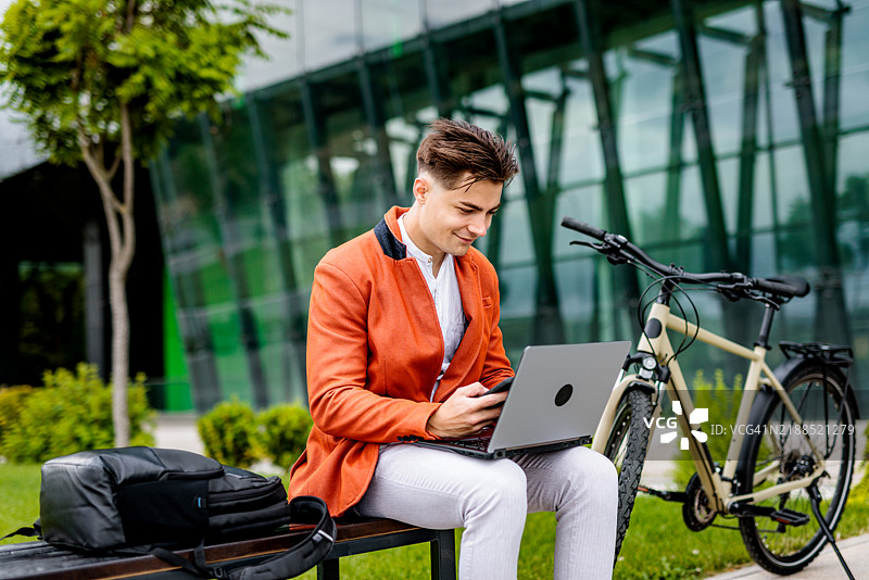 满意的年轻商人在公园里使用笔记本电脑工作图片素材