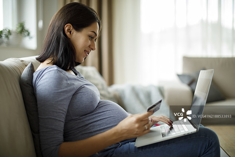 微笑的孕妇正在用信用卡网上购物图片素材