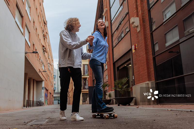 年轻男子在城市街道上帮助女友学习滑板图片素材