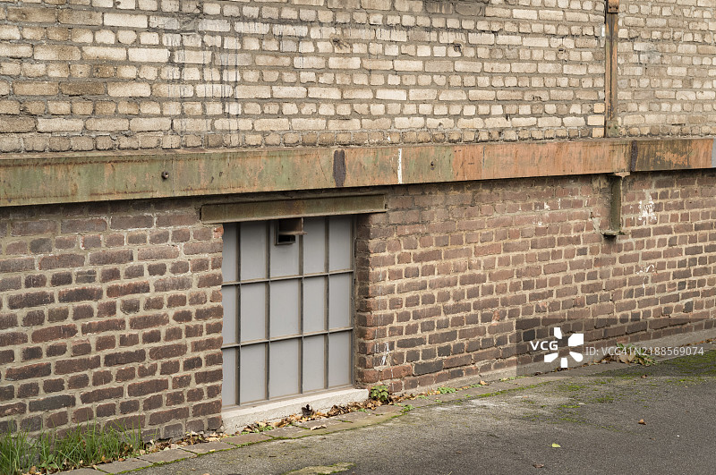 磨砂玻璃地下窗户照亮了一面风化的工业砖墙建筑，展示了城市衰败和建筑纹理。图片素材