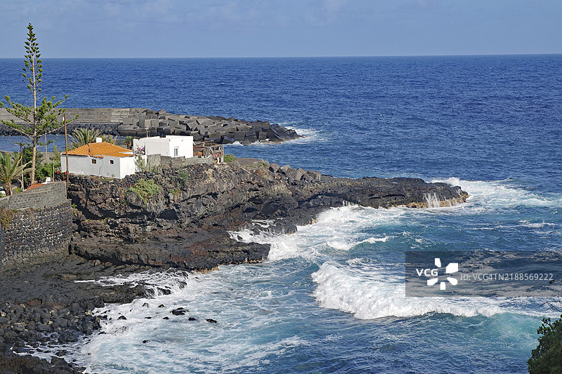 波浪拍打着岩石海岸，背景是白色房屋，位于西班牙加那利群岛拉帕尔马的圣安德烈斯。图片素材