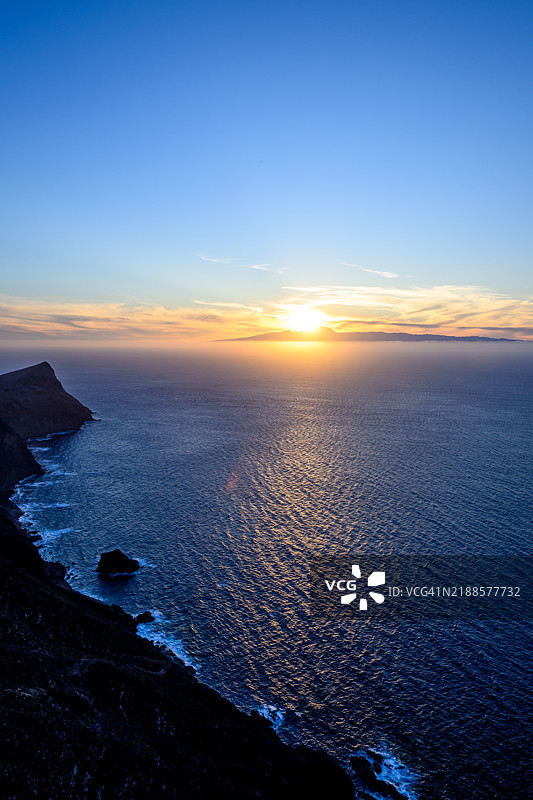 金色日落照耀着平静的海洋和崎岖的格兰 Canaria 海岸线，远处是特内里费岛。图片素材