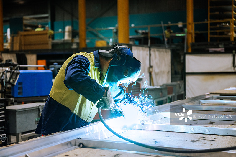 穿着防护装备的工人在工业厂房内焊接金属，四周飞溅的火花明亮地照亮了整个区域。图片素材