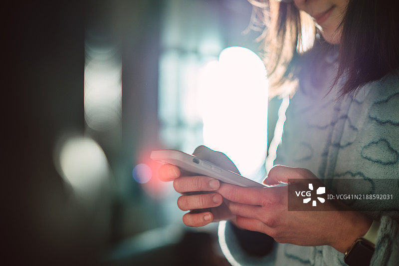柔和环境光下，女性使用智能手机的特写镜头图片素材