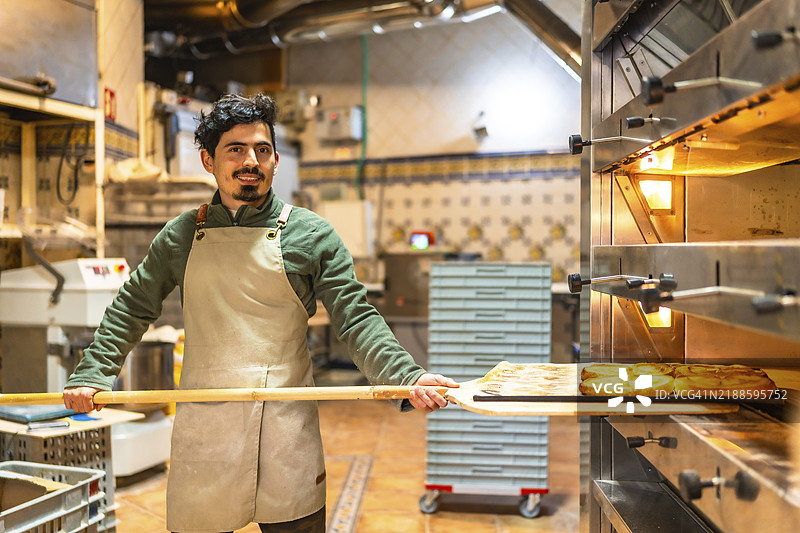 男性拉丁裔面包师正在用铲子从传统烤箱中取出美味的泡芙糕点图片素材