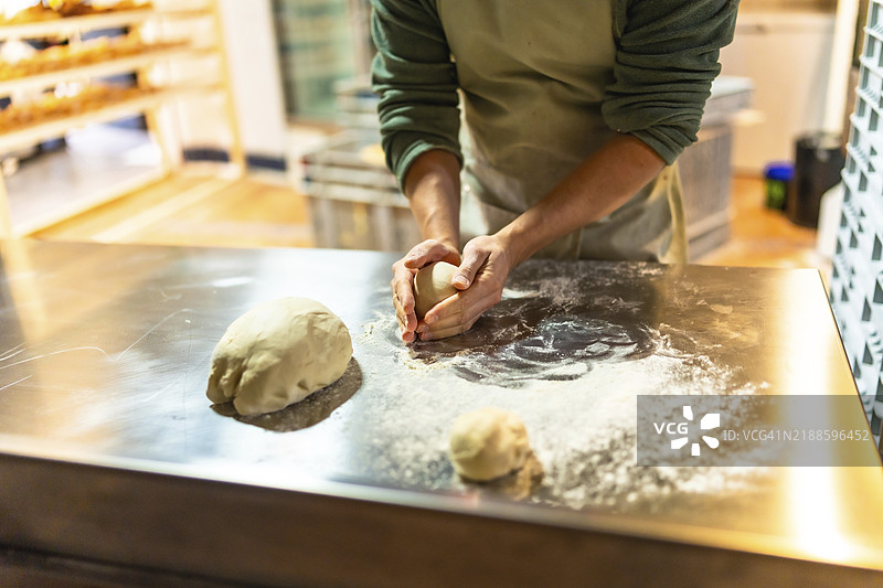 拉丁裔男性面包师在手工面包店的工作坊中揉面团的特写镜头图片素材