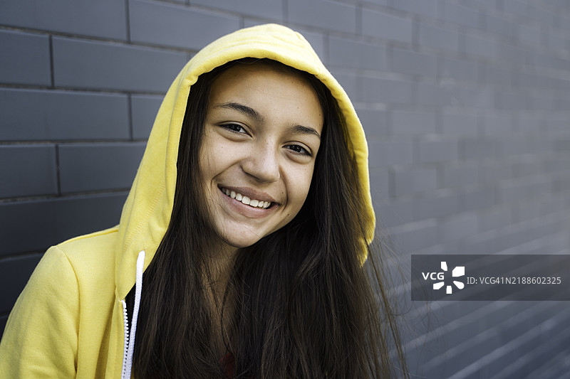 穿着黄色连帽外套的微笑女孩户外肖像图片素材