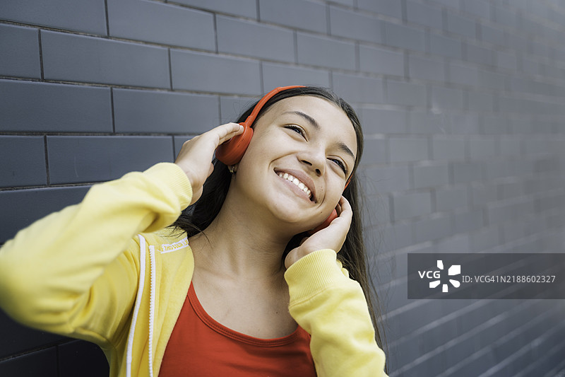 活泼的年轻女孩戴着耳机，开心地微笑图片素材