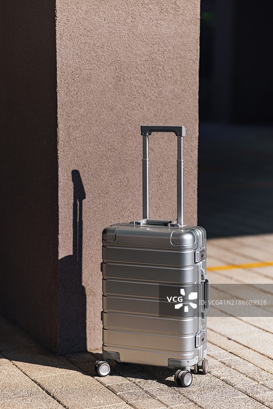 光滑的银色行李箱靠在墙上，沐浴在户外自然阳光下图片素材