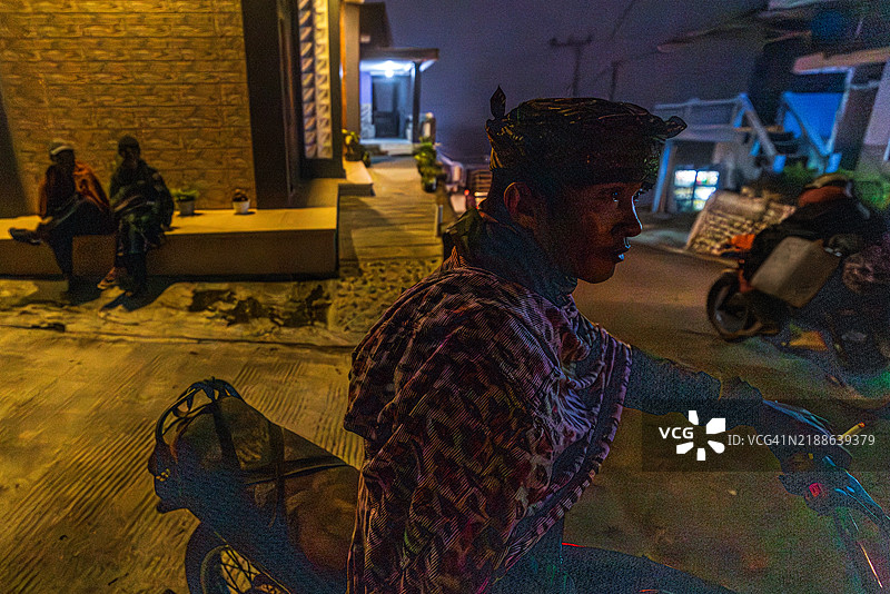 在夜晚，一名男子在印度尼西亚爪哇岛的布罗莫镇骑着摩托车，抽着香烟。图片素材