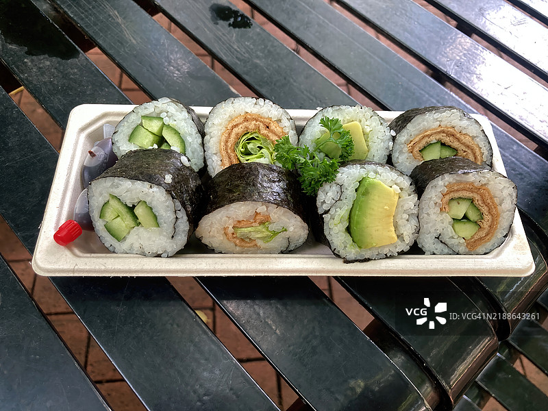 各种素食寿司，配有鳄梨、黄瓜和豆腐，放在户外野餐桌上的纸板外卖托盘上图片素材
