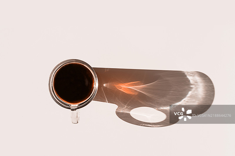 香气四溢的早晨咖啡在玻璃杯中，杯子在米色背景上投下长长的影子。2025年流行色摩卡慕斯。图片素材