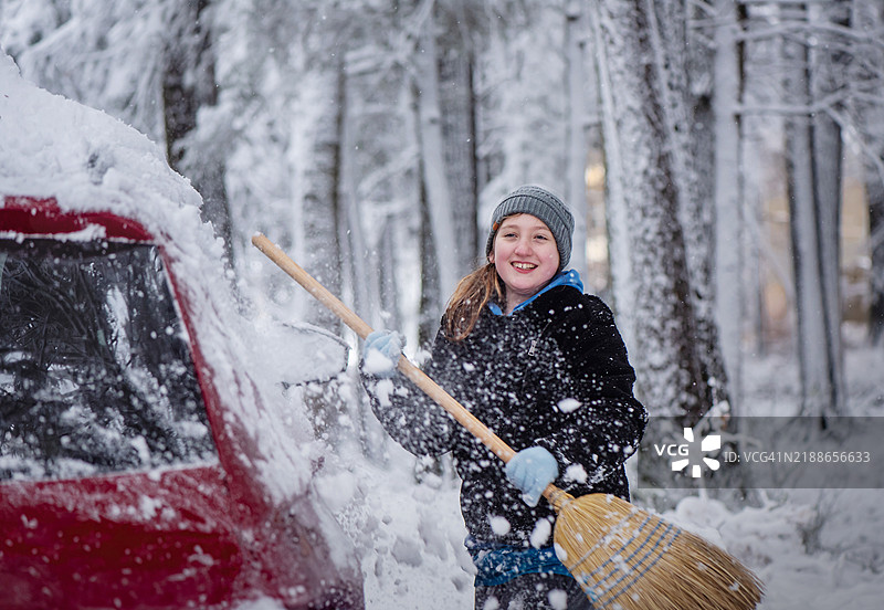 清理家庭汽车上的雪。一个11岁的女孩参与冬季任务。图片素材