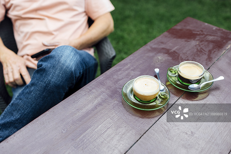 一个无法辨认的男人在户外放松，手边的木桌上放着咖啡图片素材