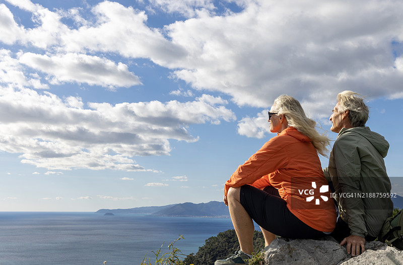 成熟的情侣坐在山顶上眺望大海图片素材