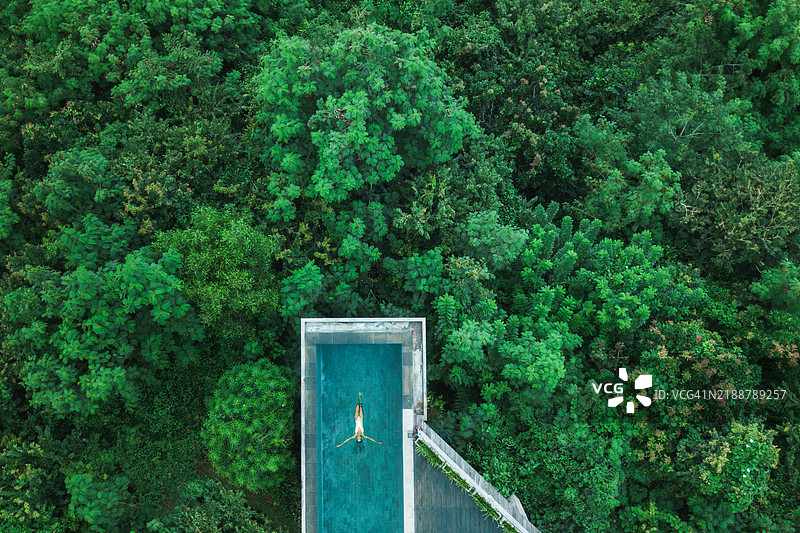 无人机航拍的女子在丛林中隐秘的无边泳池中放松。图片素材