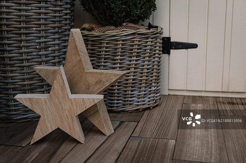 木制星星靠近装有香桃木植物和松果的藤编篮子。图片素材