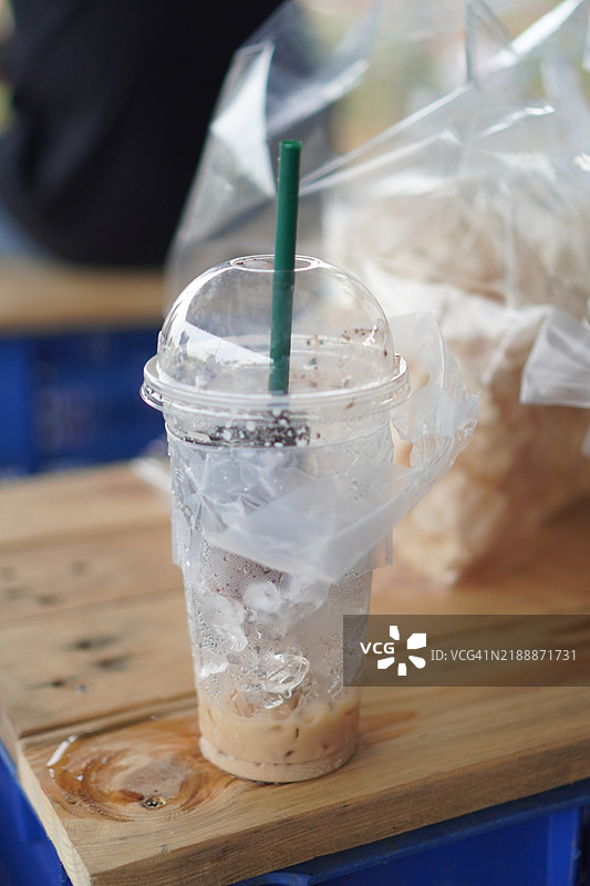 黑色冰茶饮料放在透明塑料杯中，置于木桌上。图片素材