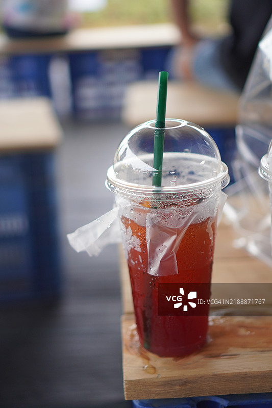 黑色冰茶饮料放在透明塑料杯中，置于木桌上。图片素材