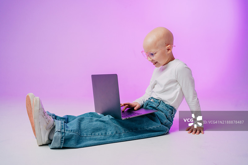 微笑的光头儿童戴着眼镜在紫色背景下使用笔记本电脑图片素材