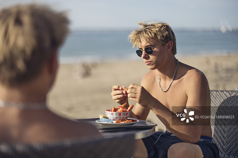 青少年男孩在海滩上享受一碗虾。图片素材