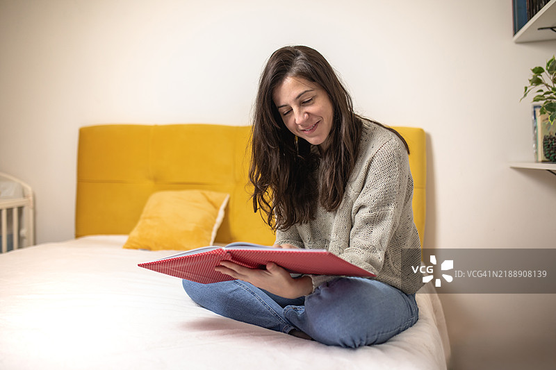 年轻漂亮的女人坐在床上翻看相册。图片素材