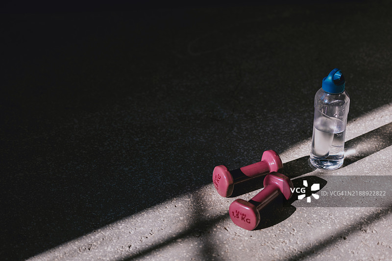 阳光照射下的健身房地板上的粉色哑铃和水瓶图片素材