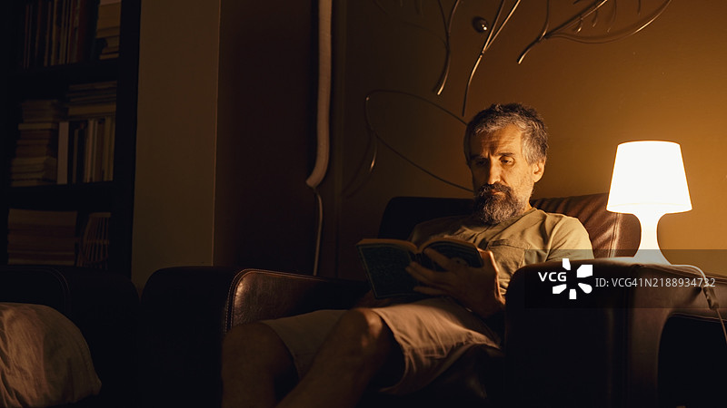 成熟男性在深夜阅读一本书。放松在家。图片素材