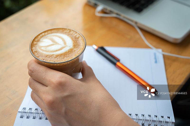 有人在开始工作前手持热拿铁咖啡的特写镜头。图片素材