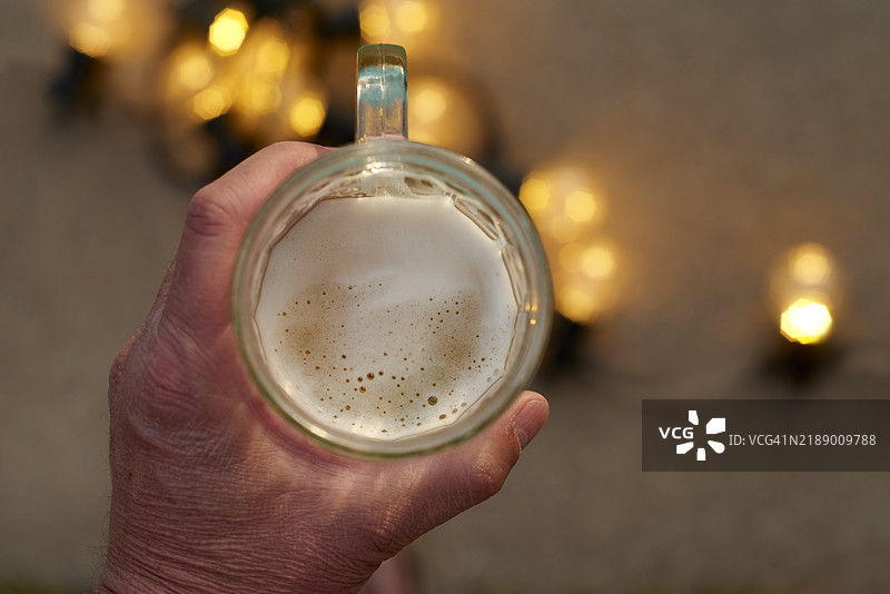 手握啤酒杯，背景是串灯。图片素材