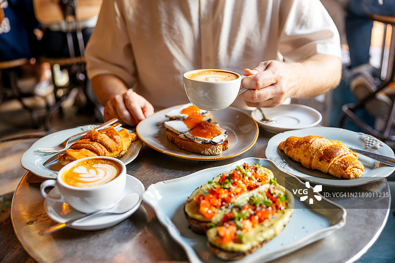 男子在咖啡馆享用牛油果吐司、可颂和咖啡的早餐图片素材