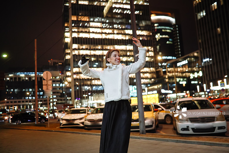 在城市中跳舞：一位穿着温暖衣物的女性在夜晚的城市街道上表演巴查塔舞。图片素材