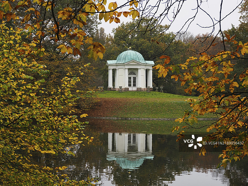 卡尔萨乌的天鹅岛上的寺庙，四周环绕着秋天的树木，树木的倒影映在宁静的水面上，德国黑森州卡塞尔，欧洲图片素材