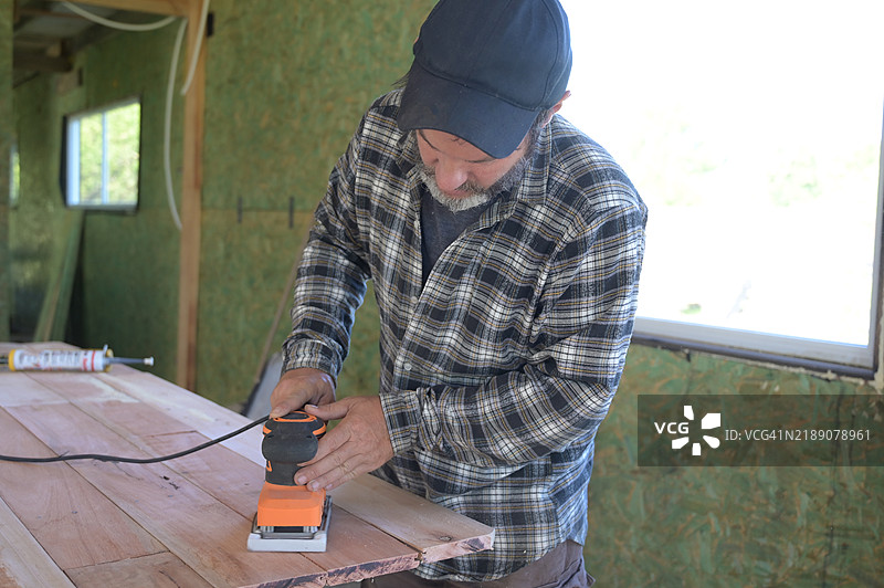 男子在木材上使用圆盘砂光机。图片素材